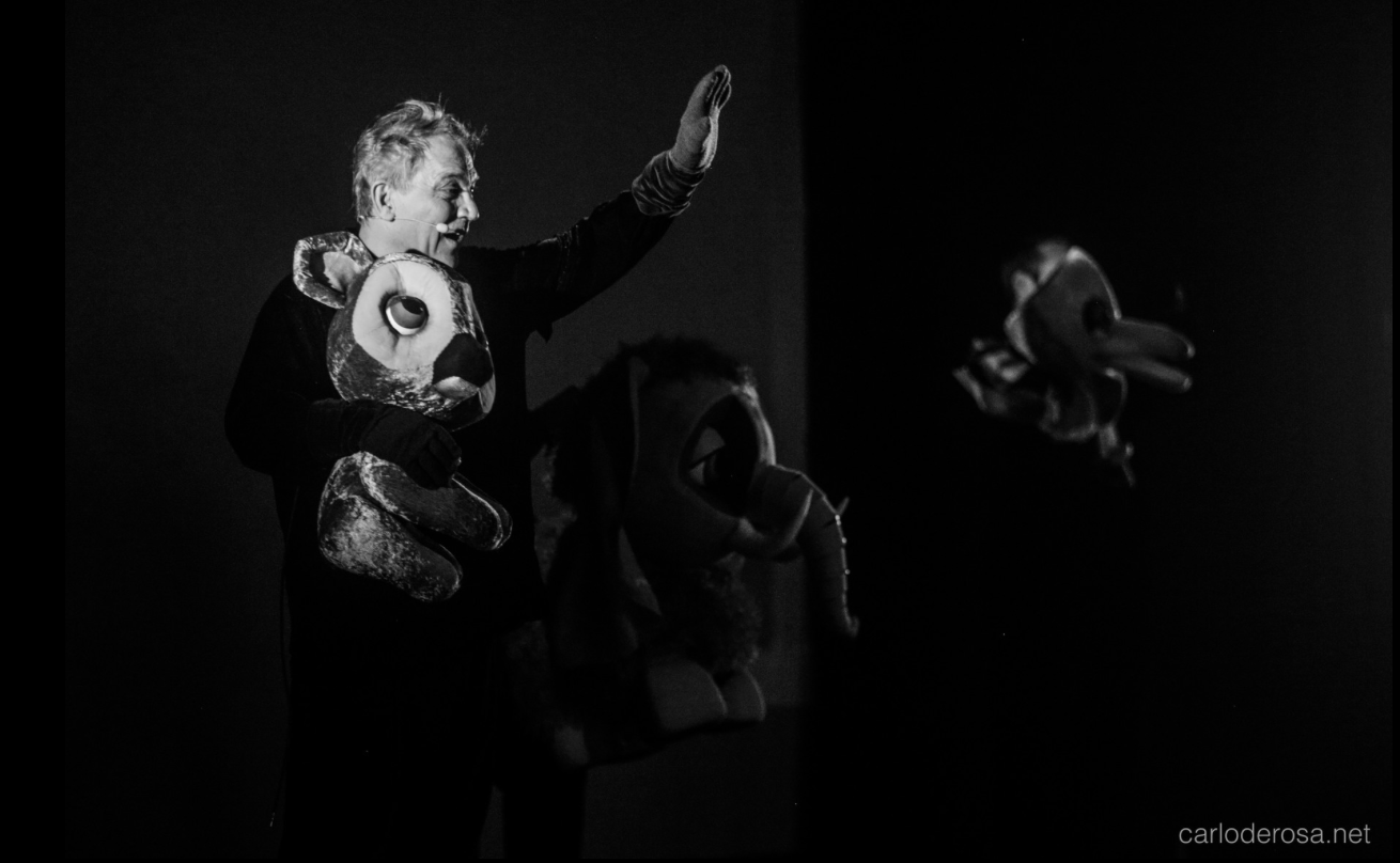 Photographie en noir et blanc d’un marionnettiste qui anime un oiseau sur scène.